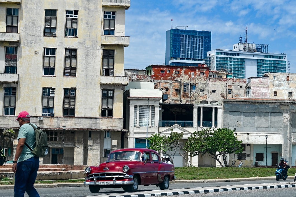 Un hombre camina por una calle mientras un auto clásico pasa a su lado, con el hotel Iberostar Selection (C) y el hotel Habana Libre Melia (D) al fondo, en La Habana, el 2 de junio de 2026. El grupo hotelero español Iberostar se ha retirado de la gestión de una docena de hoteles en Cuba que operaba en asociación con el conglomerado Gaesa, vinculado al ejército y sujeto a sanciones estadounidenses, según informaron a la AFP varias fuentes cercanas al asunto el 2 de junio de 2026. (Foto de ADALBERTO ROQUE / AFP)