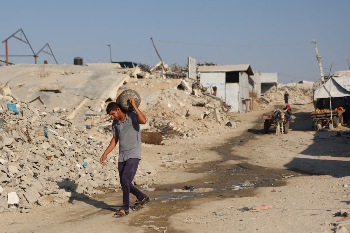 Un palestino que lleva un cilindro camina junto a los escombros de los edificios destruidos en el campamento de refugiados palestinos de Jabalia, en el norte de la Franja de Gaza, el 2 de agosto de 2026. (Omar AL-QATTAA / AFP)