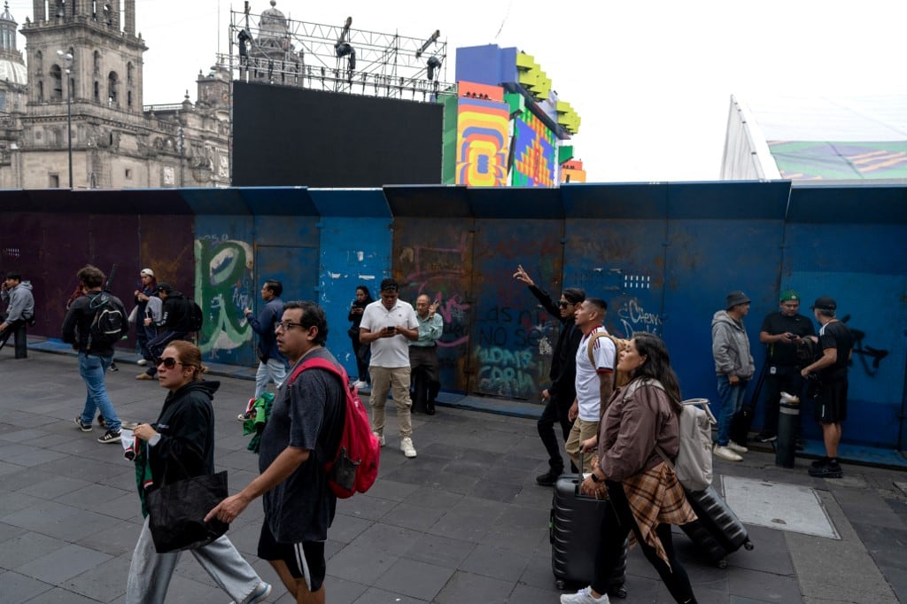 Varias personas pasan junto a una barrera de seguridad del FIFA Fan Fest en la Plaza del Zócalo, un día antes de la inauguración del Mundial de Fútbol de la FIFA 2026 en la Ciudad de México, el 10 de junio de 2026. (Foto de Gerardo Luna / AFP)