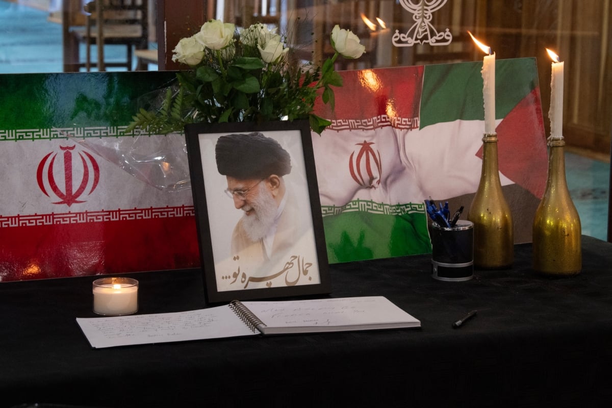 Un retrato del líder supremo de Irán, el ayatolá Ali Jameneí, se exhibe junto a banderas iraníes, velas y un libro de condolencias en el complejo de la mezquita Ahlul Bait, mientras los fieles musulmanes rezan en su memoria en Ciudad del Cabo el 1 de marzo de 2026. (Foto: AFP)