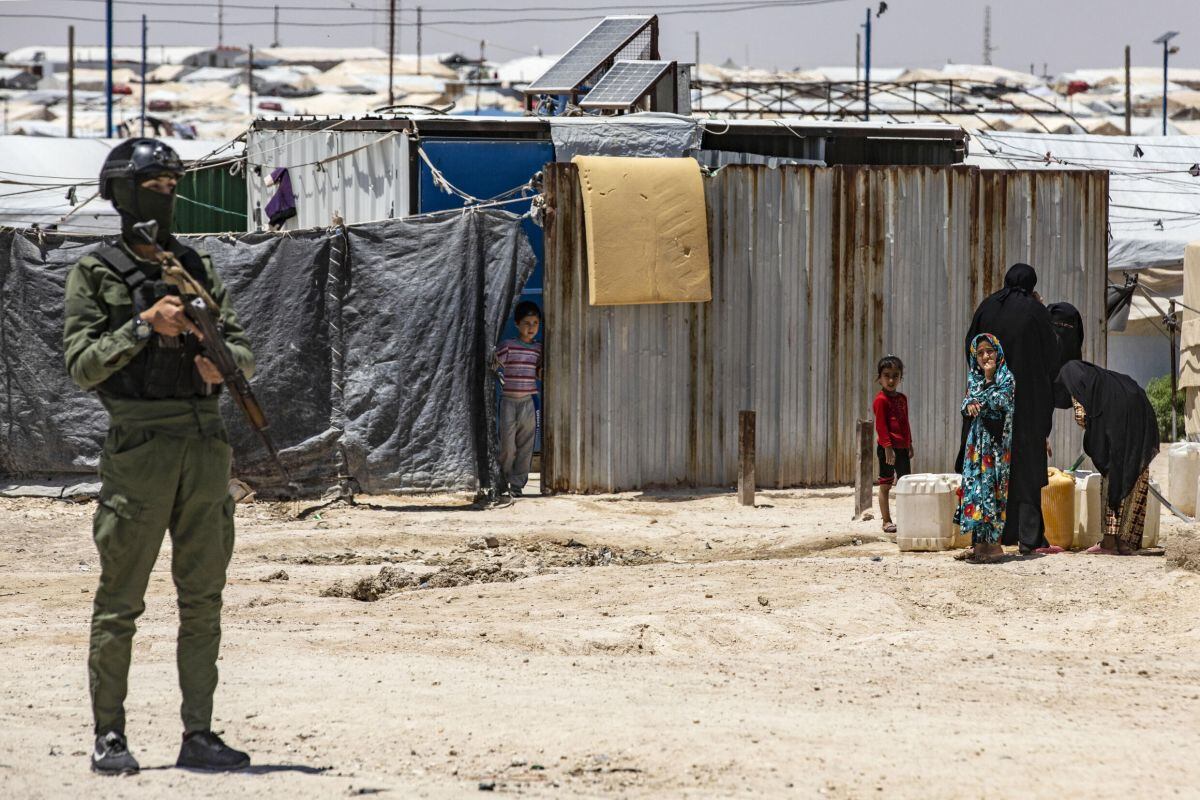 Un miembro de las fuerzas de seguridad kurdas monta guardia mientras unas mujeres y unos niños llenan bidones de agua en el campamento de Al Hol, en el noreste de Siria|Foto: Delil Souleiman / AFP