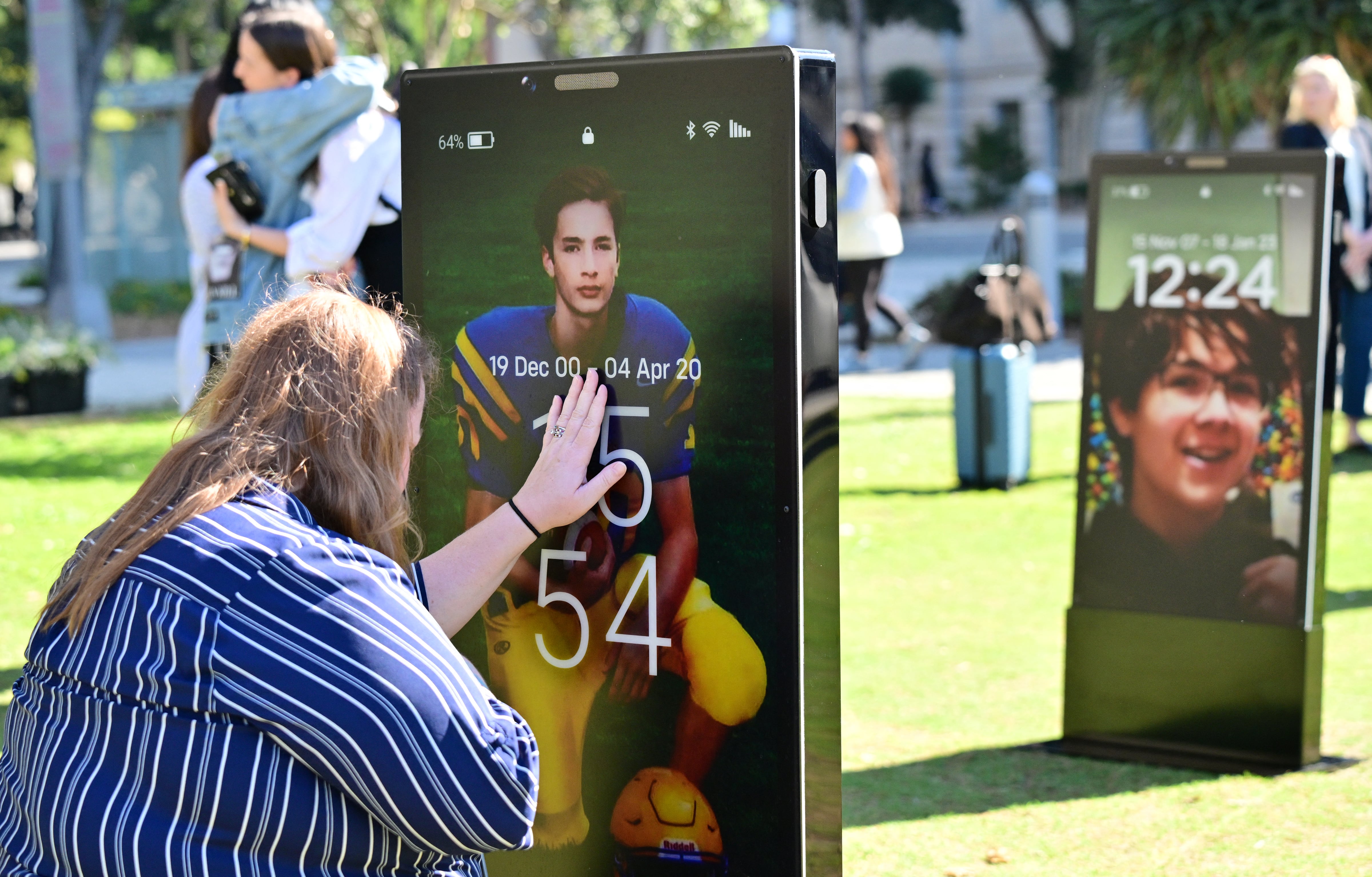 Padres afligidos observan imágenes de sus hijos fallecidos en el "Monumento a las Pantallas Perdidas", una instalación artística de teléfonos inteligentes a gran escala que muestra a 50 niños que perdieron la vida debido a los peligros de internet, en Los Ángeles, California, el 13 de febrero de 2026. Meta y YouTube, propiedad de Google, fueron acusadas el 9 de febrero de 2026 de promover aplicaciones altamente adictivas entre los niños, al tiempo que comenzaba formalmente un histórico juicio sobre redes sociales en un tribunal de California. (Foto de Frederic J. BROWN / AFP)