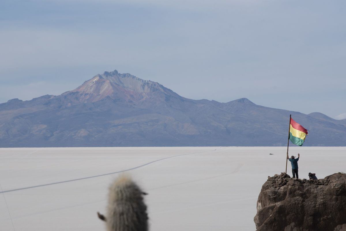 Una persona posa junto a una bandera boliviana en la Isla Incahuasi mientras el volcán Tunupa se alza sobre el Salar de Uyuni en Potosí, Bolivia, el martes 10 de diciembre de 2019.