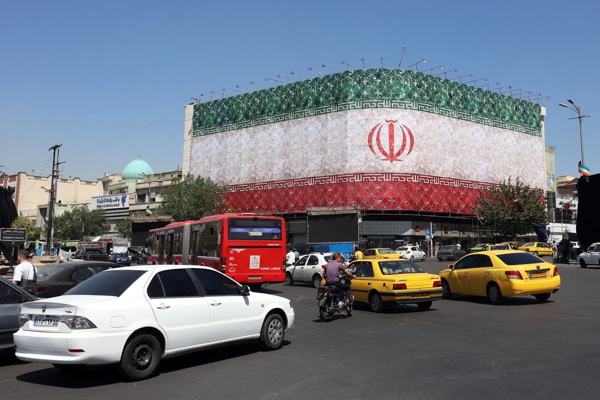 El tráfico circula junto a la bandera nacional iraní que ondea en un edificio de la plaza Enghelab en Teherán, el 14 de junio de 2026. (AFP)