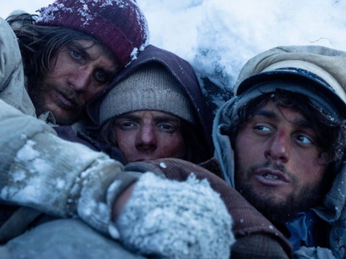 Tres protagonistas de la película "La sociedad de la nieve" en medio de los Andes, protegiéndose del frío tras el accidente aéreo (Foto: Netflix)