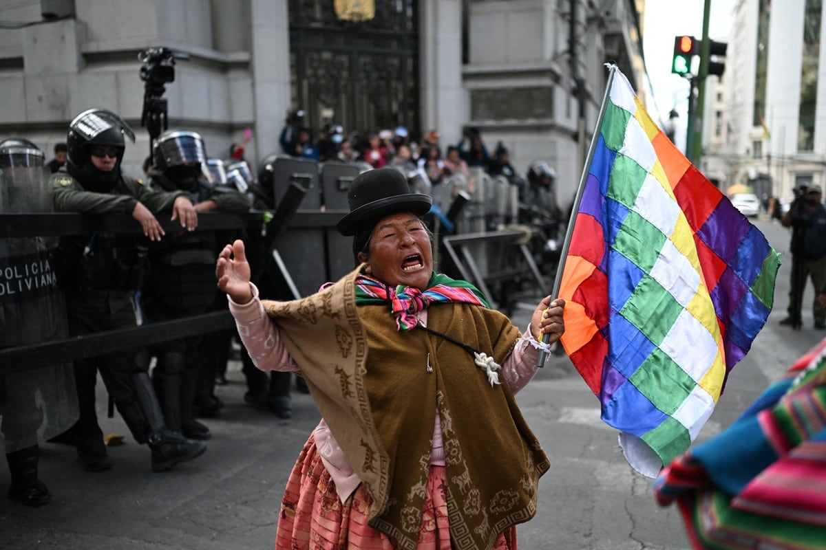 Una mujer indígena que sostiene una bandera Wiphala hace un gesto frente a la policía antidisturbios durante una protesta contra el gobierno del presidente Rodrigo Paz en el Día de la Madre en La Paz, el 27 de mayo de 2026. (Marvin RECINOS / AFP)