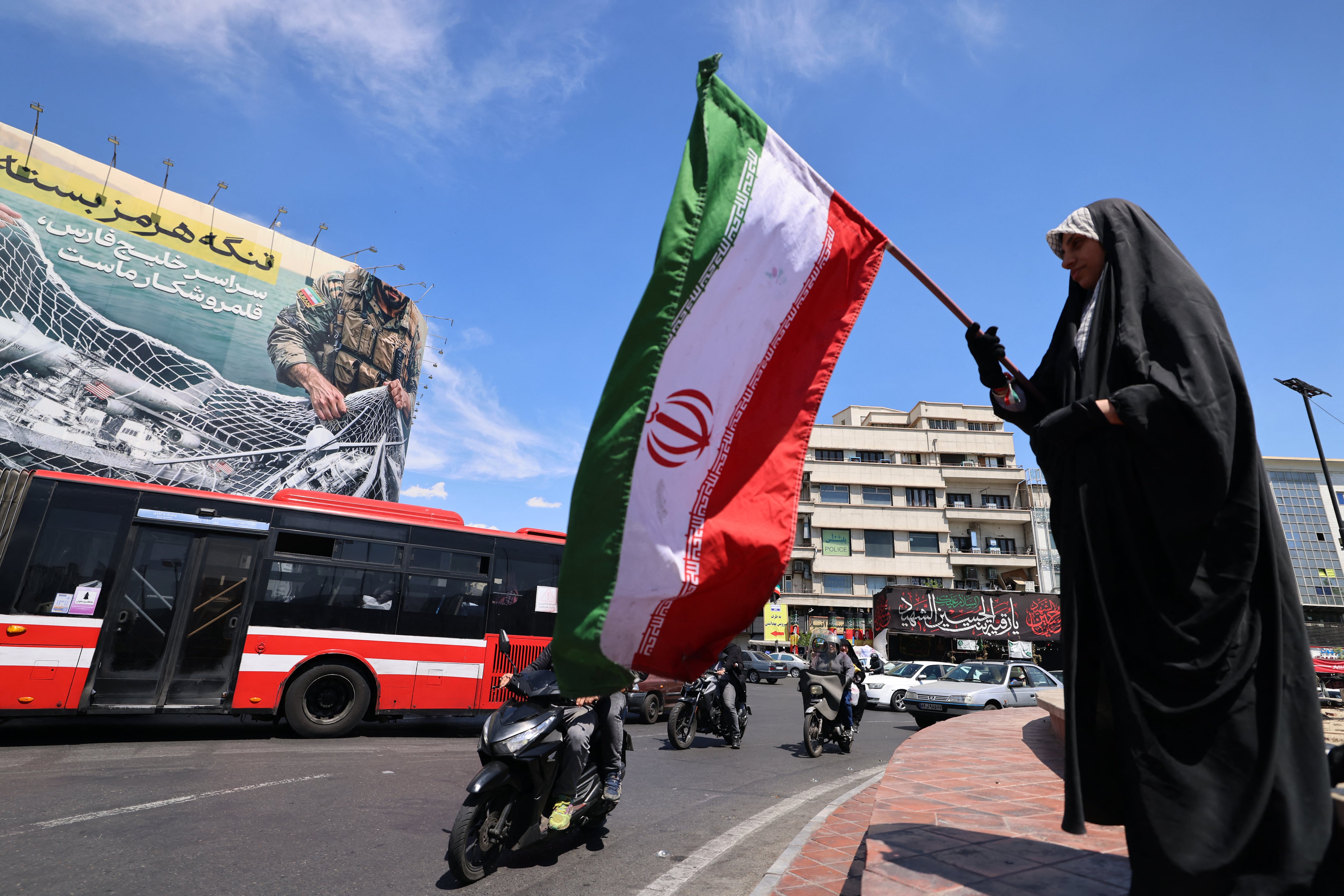 Una mujer ondea la bandera de Irán frente a una valla publicitaria gigante que dice "El estrecho de Ormuz permanece cerrado", en la Plaza de la Revolución de Teherán, el 12 de abril de 2026. (Foto de ATTA KENARE / AFP).