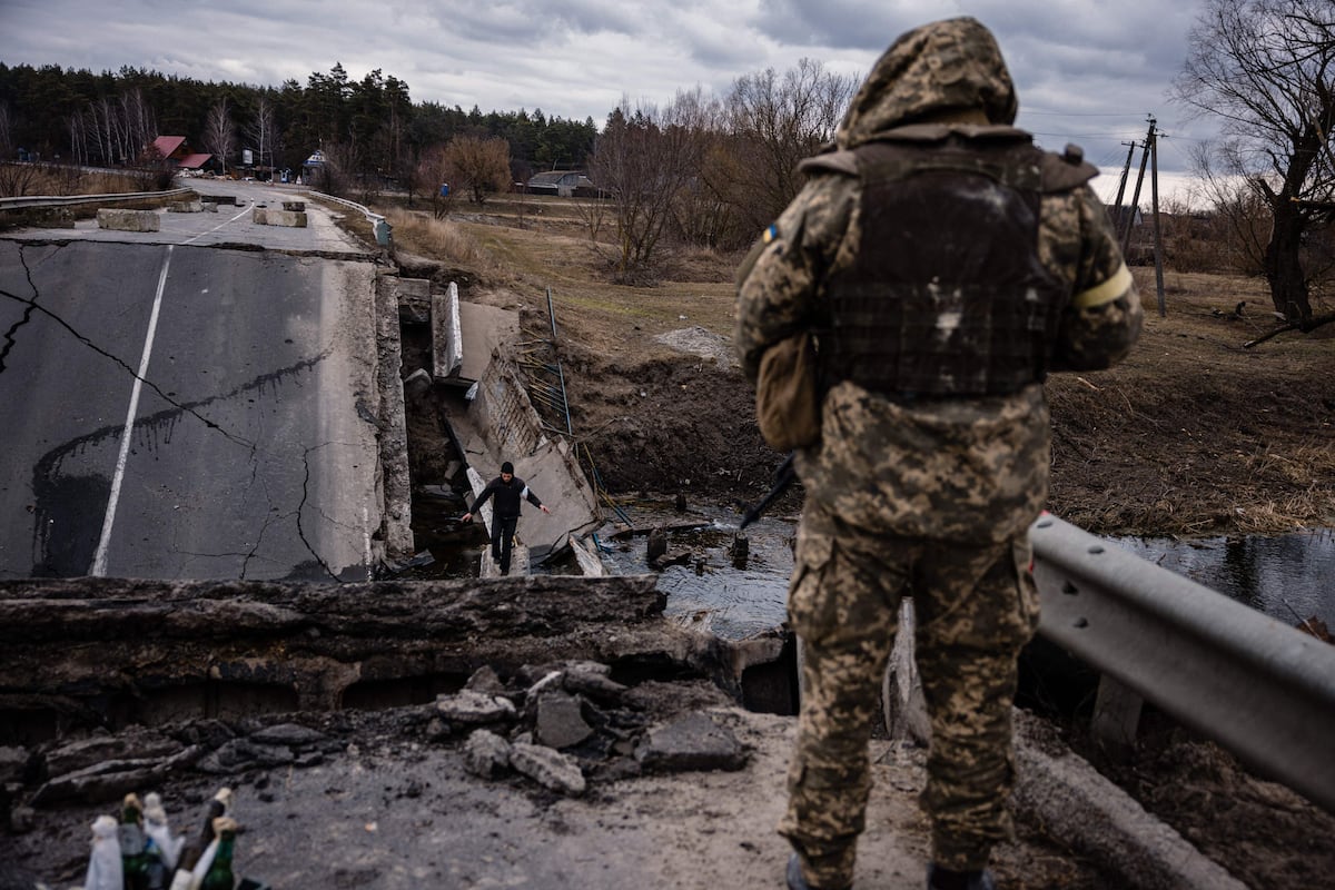 Un militar ucraniano mira a un civil que cruza un puente volado en una aldea, al este de la ciudad de Brovary, el 6 de marzo de 2022. (Foto: Dimitar DILKOFF / AFP)