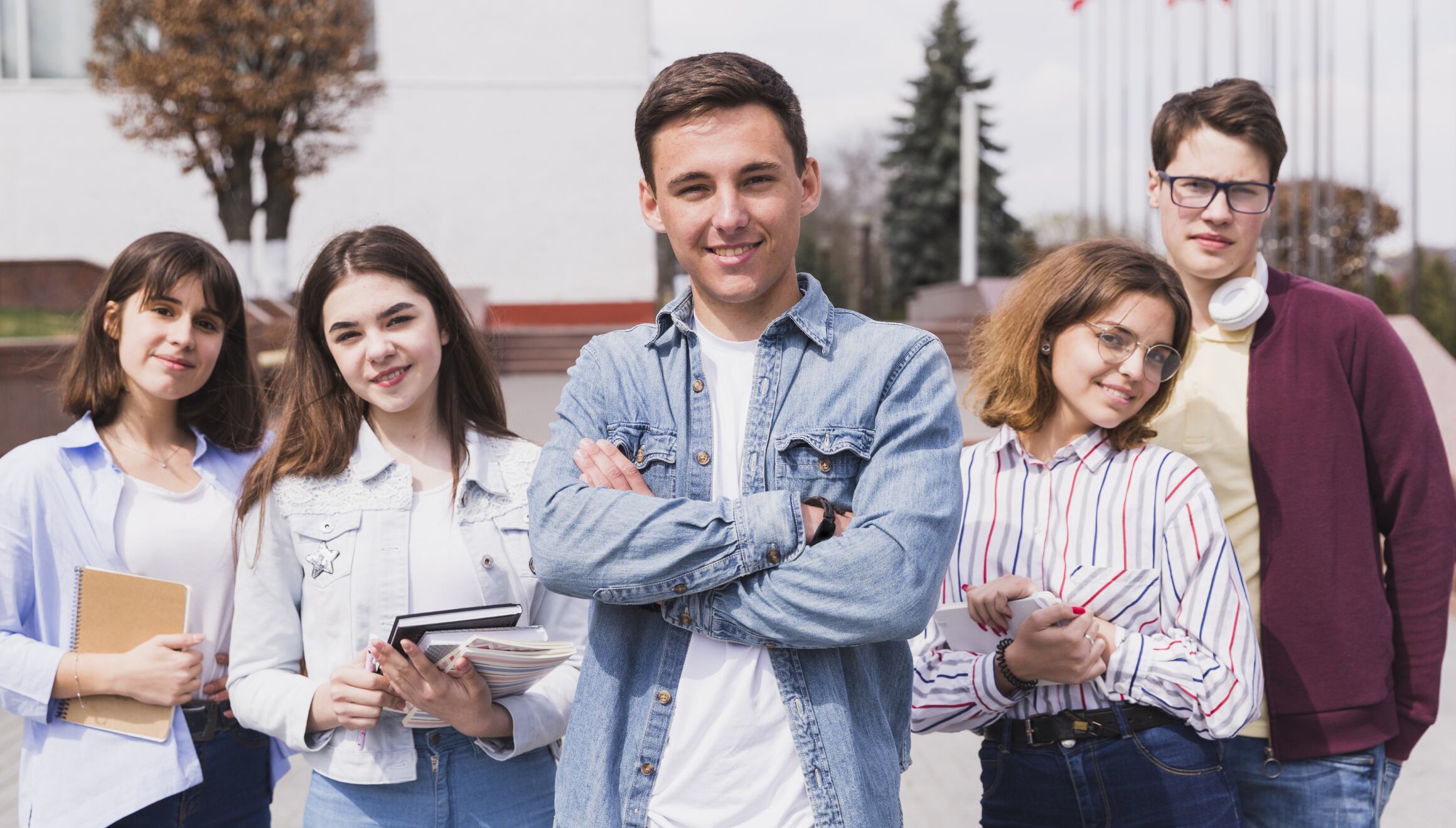 Cinco estudiantes universitarios mirando a la cámara mientras algunos sostienen sus libros y apuntes de sus clases universitarias (Foto: Freepik)