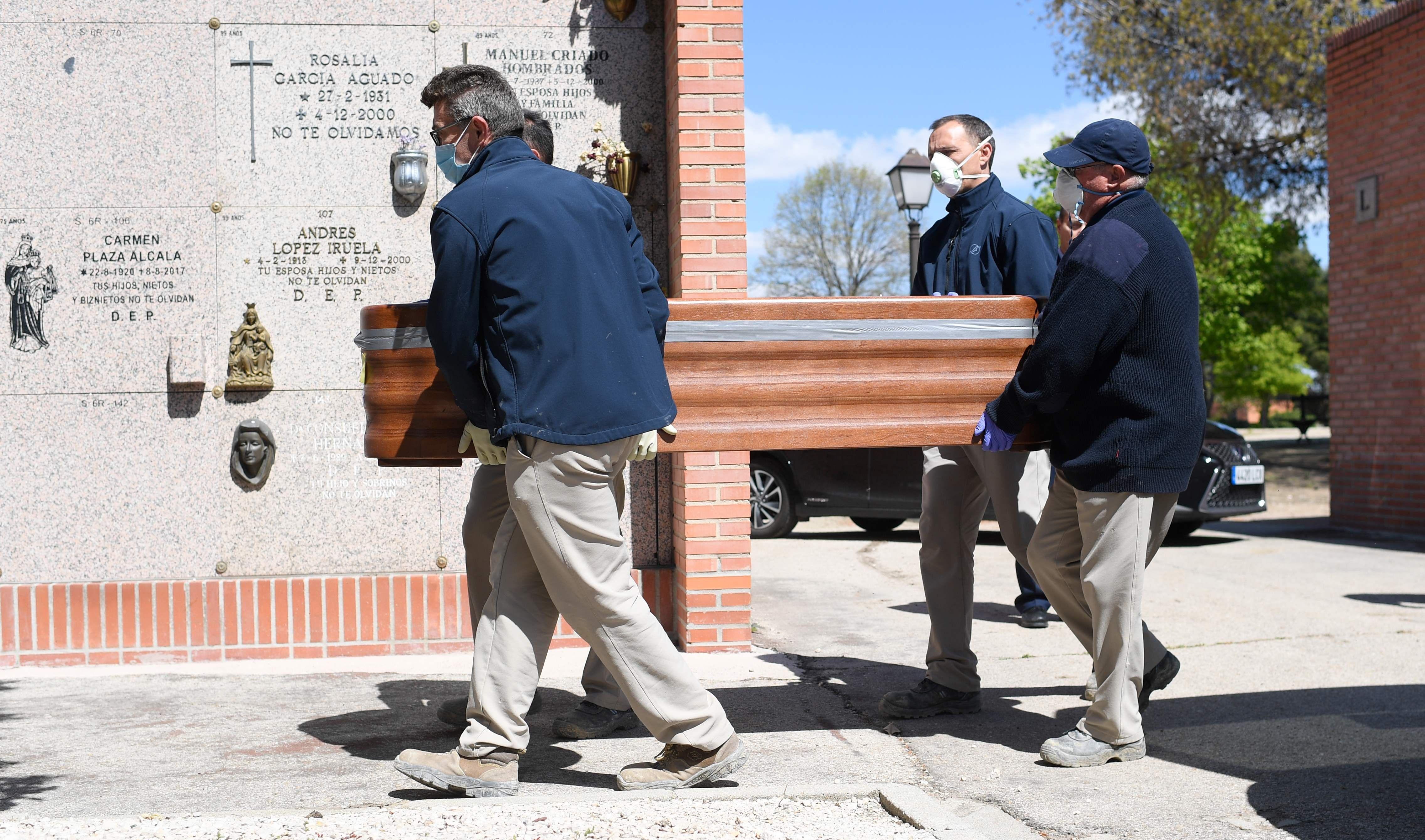 Trabajadores de una funeraria llevan el ataúd de una víctima de coronavirus en un cementerio de Madrid. (AFP / OSCAR DEL POZO).
