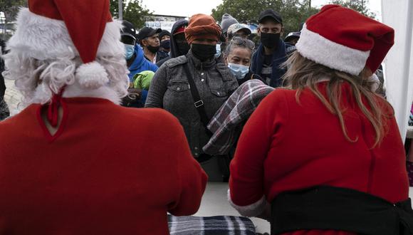 Voluntarios disfrazados de Papá Noel entregan mantas a las personas que asisten a un evento benéfico realizado por ONG en apoyo a migrantes y grupos vulnerables en Tijuana, México. (Foto: Guillermo Arias / AFP).
