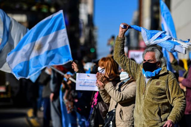 La gente ondea banderas argentinas durante una protesta contra las políticas de salud del gobierno, en relación con las estrictas medidas de bloqueo contra la propagación del nuevo coronavirus. (AFP/RONALDO SCHEMIDT).
