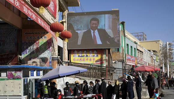 Vecinos esperando en fila en un control de seguridad en el bazar Hotan, donde una pantalla muestra al presidente de China, Xi Jinping, en Hotan, en la región occidental china de Xinjiang. (Foto: AP)