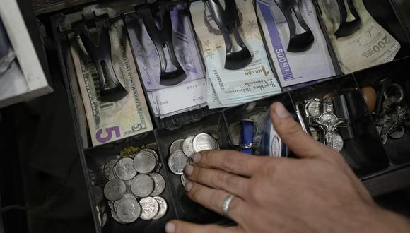 Un vendedor cuenta bolívares venezolanos y billetes de dólares estadounidenses para entregar cambio a un cliente en un mercado público en Caracas, Venezuela, el martes 18 de enero de 2022. (Foto AP/Matías Delacroix)