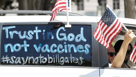 Manifestantes participan en una caravana de vehículos con un letrero que dice 'Confíe en Dios, no en las vacunas' fuera del Ayuntamiento, pidiendo a los funcionarios de California que reabran la economía en medio de la pandemia de coronavirus, el 22 de abril del 2020 en Los Ángeles, California. (Mario Tama / Getty Images)